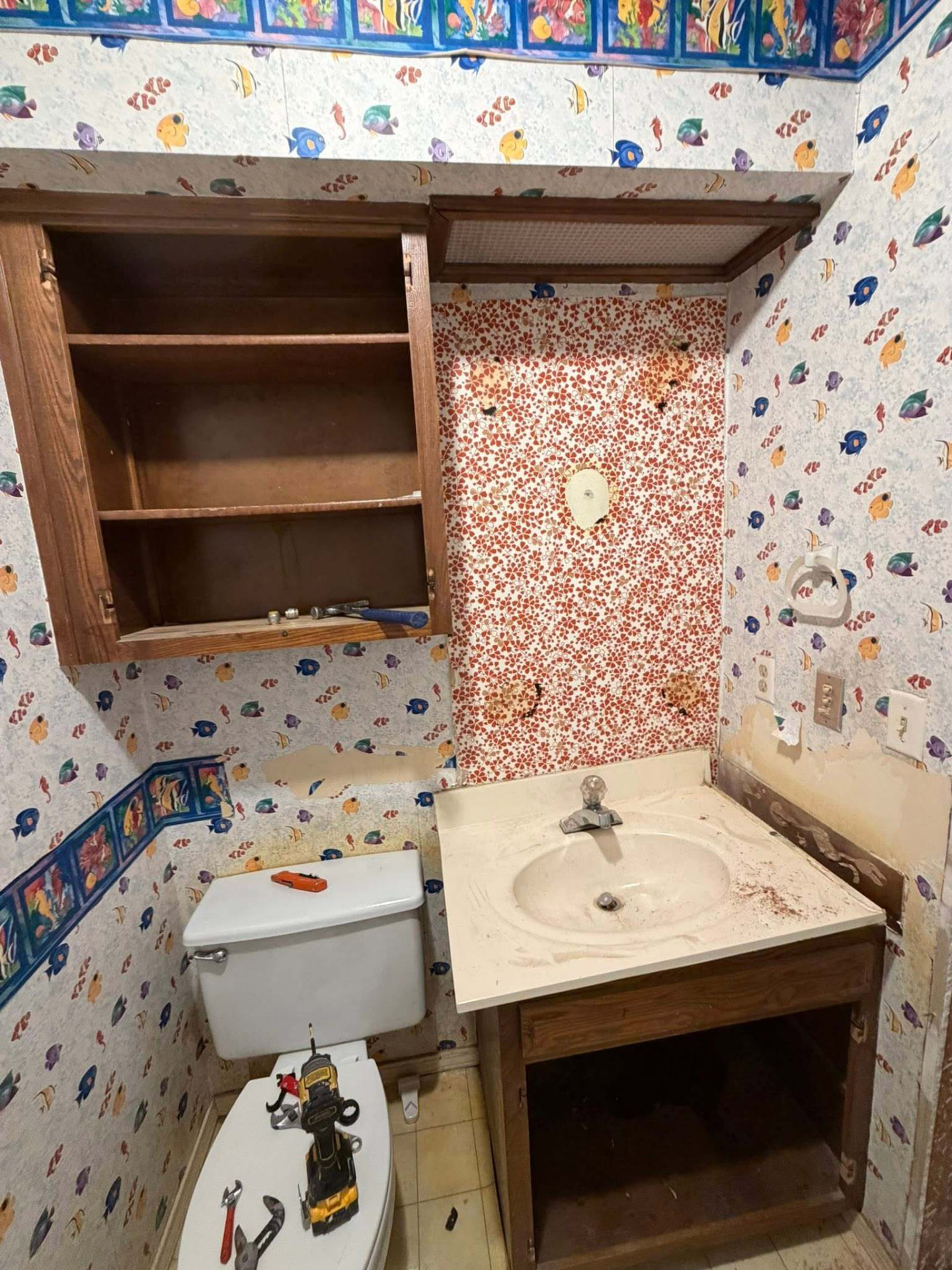 Dated bathroom before remodel with peeling fish wallpaper, worn vanity, and stained countertop