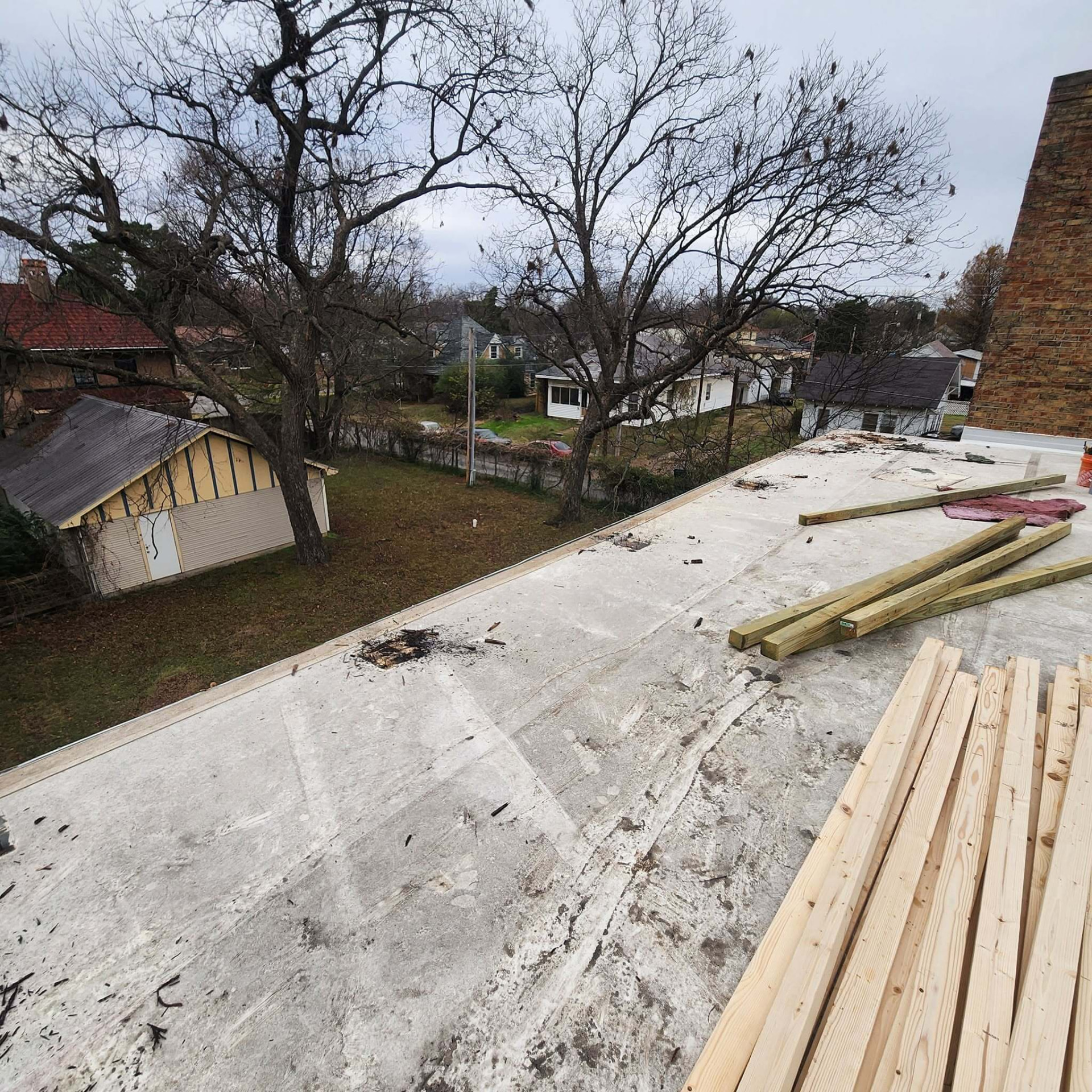 Flat roof with burn marks removed and stacks of new treated lumber staged for framing