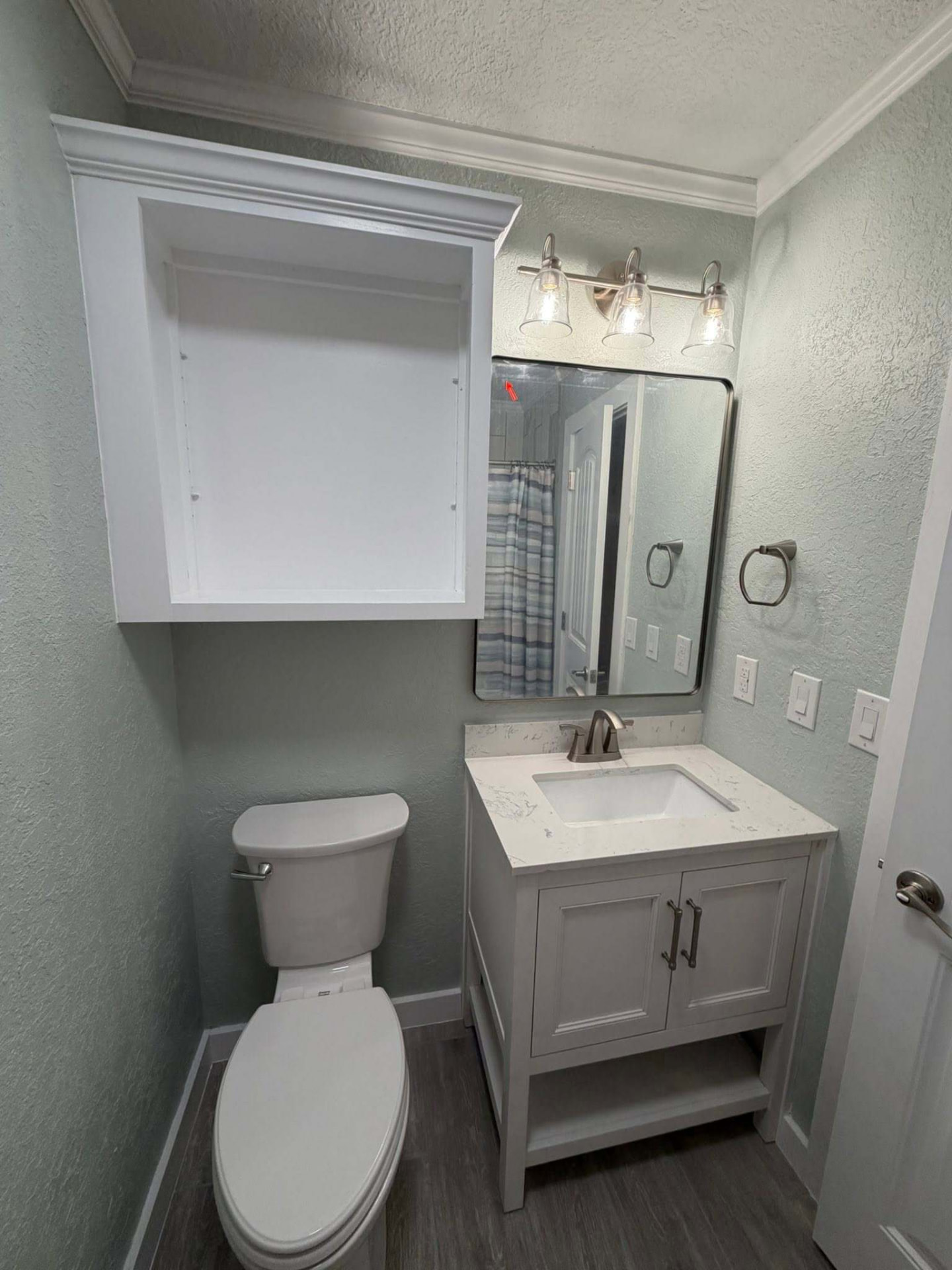 Same bathroom after rebuild with fresh paint, crown molding, new vanity, quartz top, and modern lighting