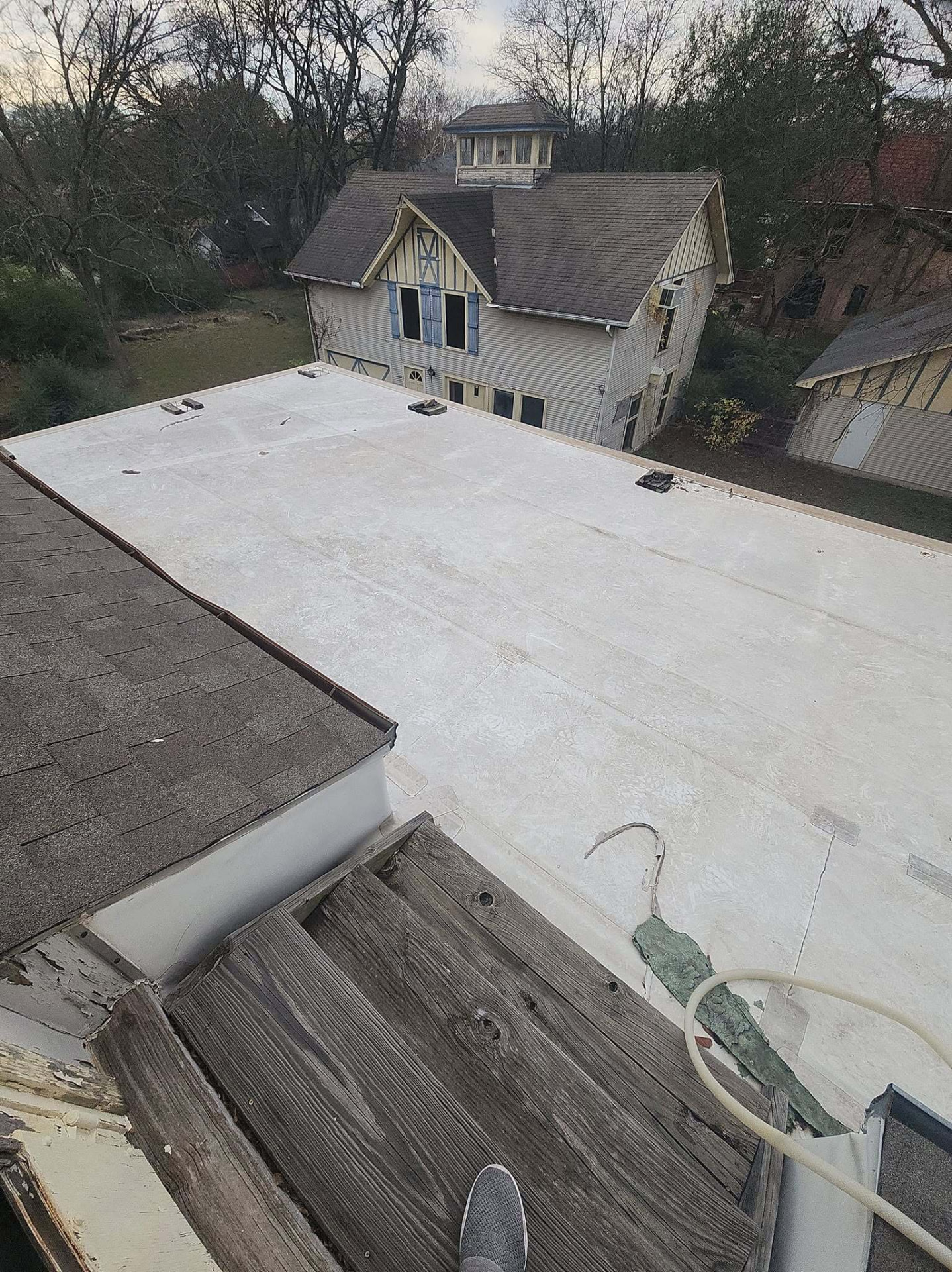 Flat roof deck surface being prepped above a two story home with a detached carriage house behind it
