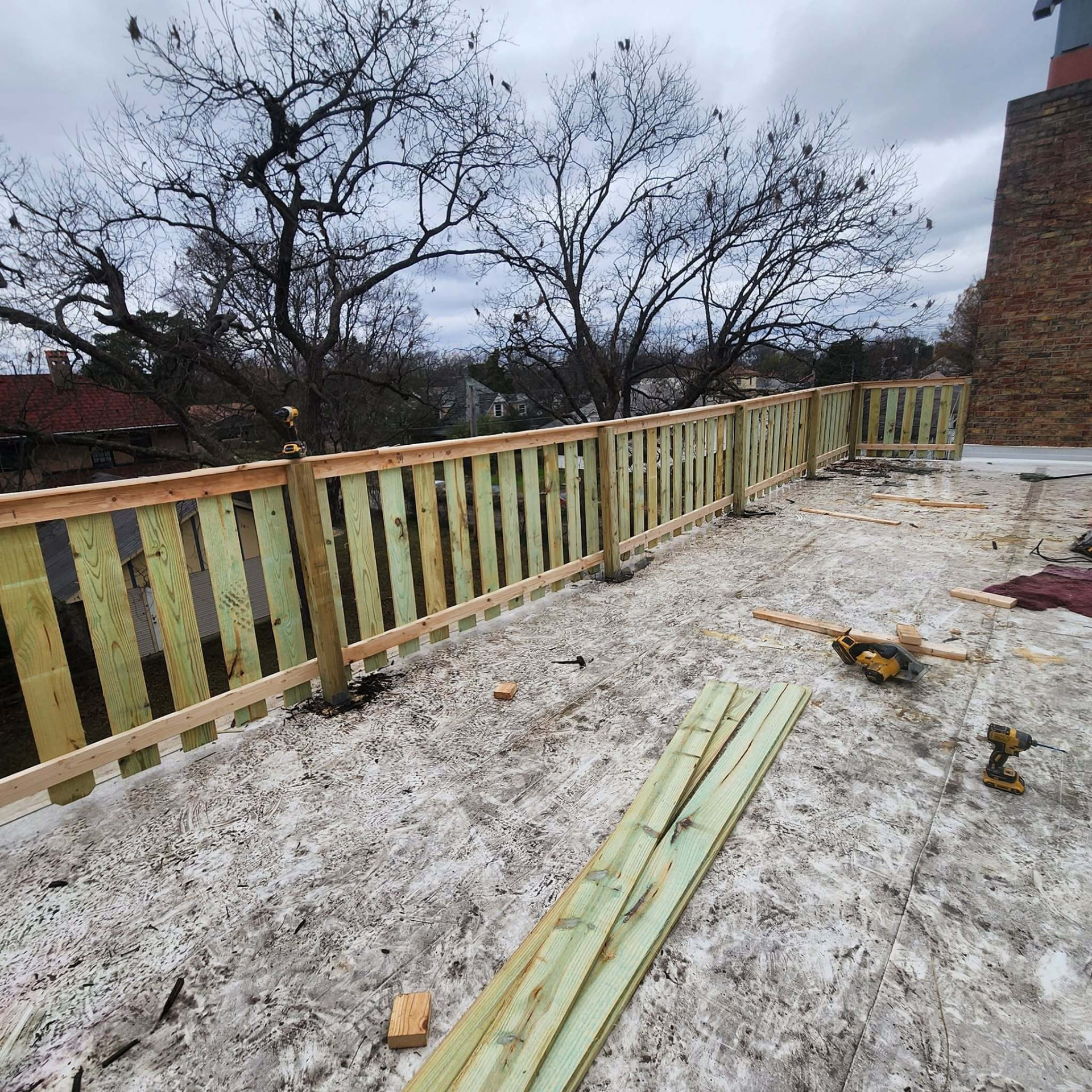 Newly framed treated wood railing running along the edge of a rooftop deck with tools on the surface